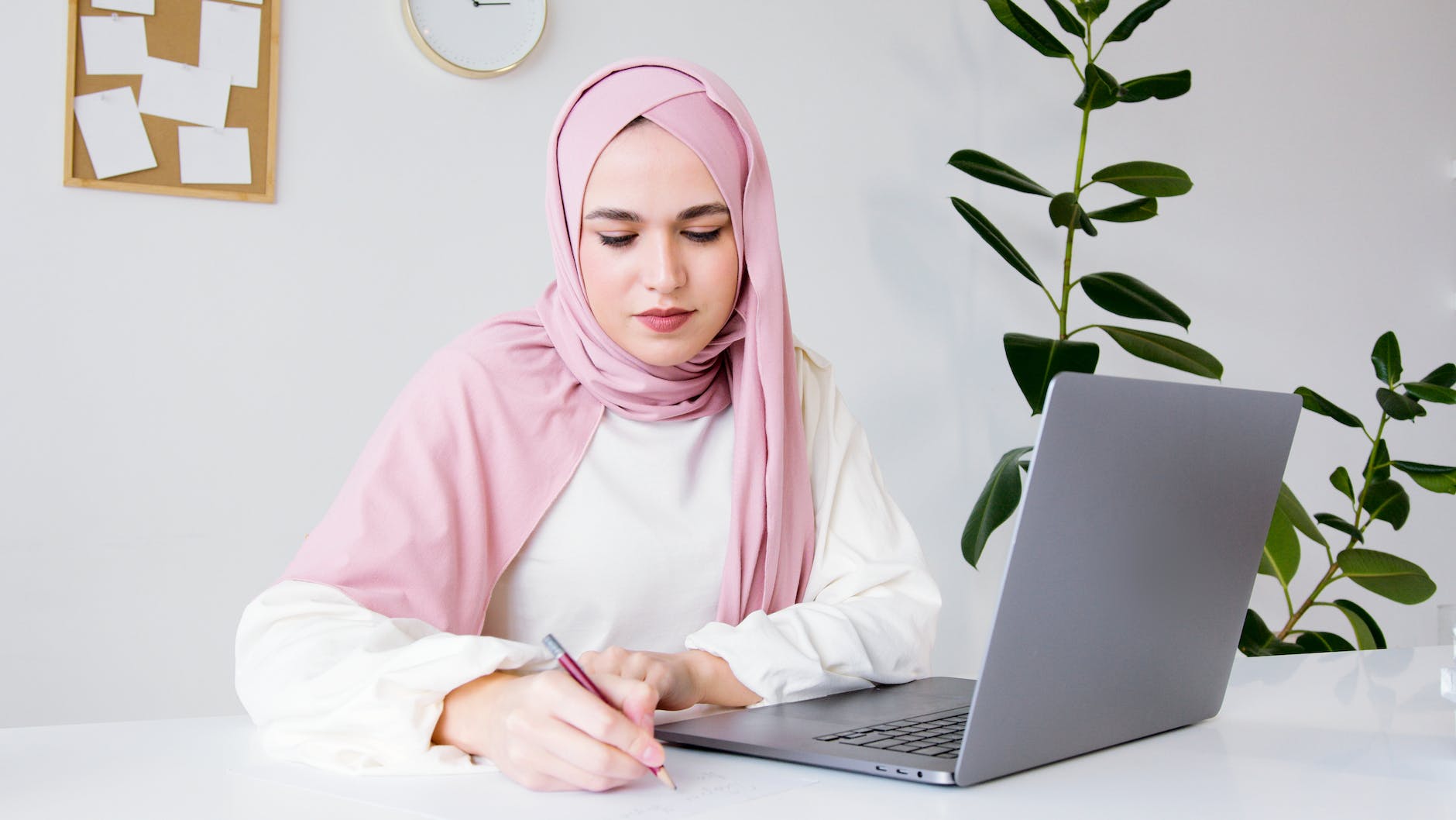 woman in white long sleeve shirt and pink hijab writing on white paper